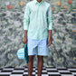 Male model wearing malmal regular fit formal shirt in mint green with striped blue shorts and hat on checkered floor