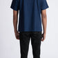 Back view of a man wearing Stylera men's blue regular fit t-shirt with black pants and white shoes