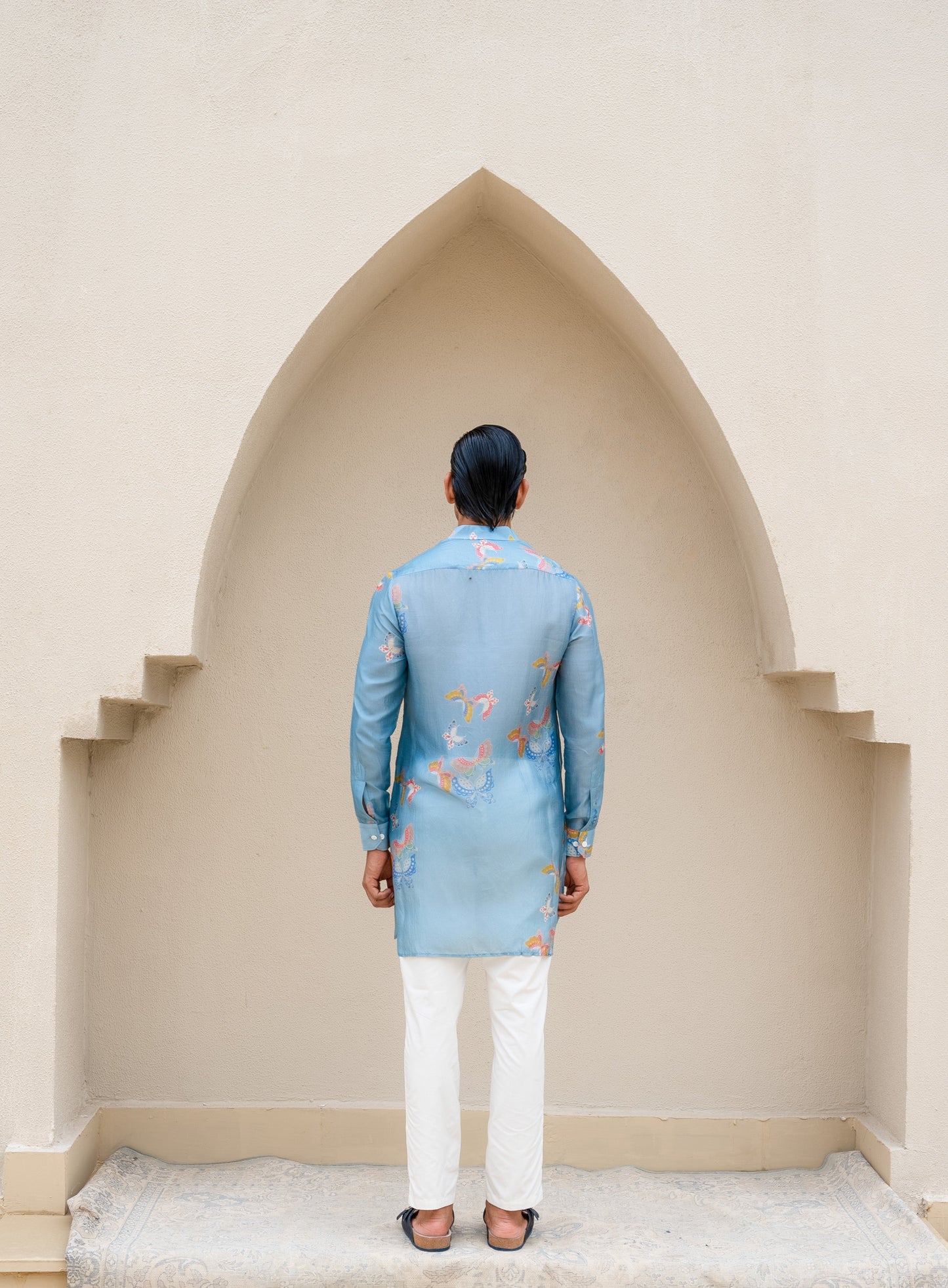 Men's printed kurta with butterfly design in blue fabric, styled with white trousers