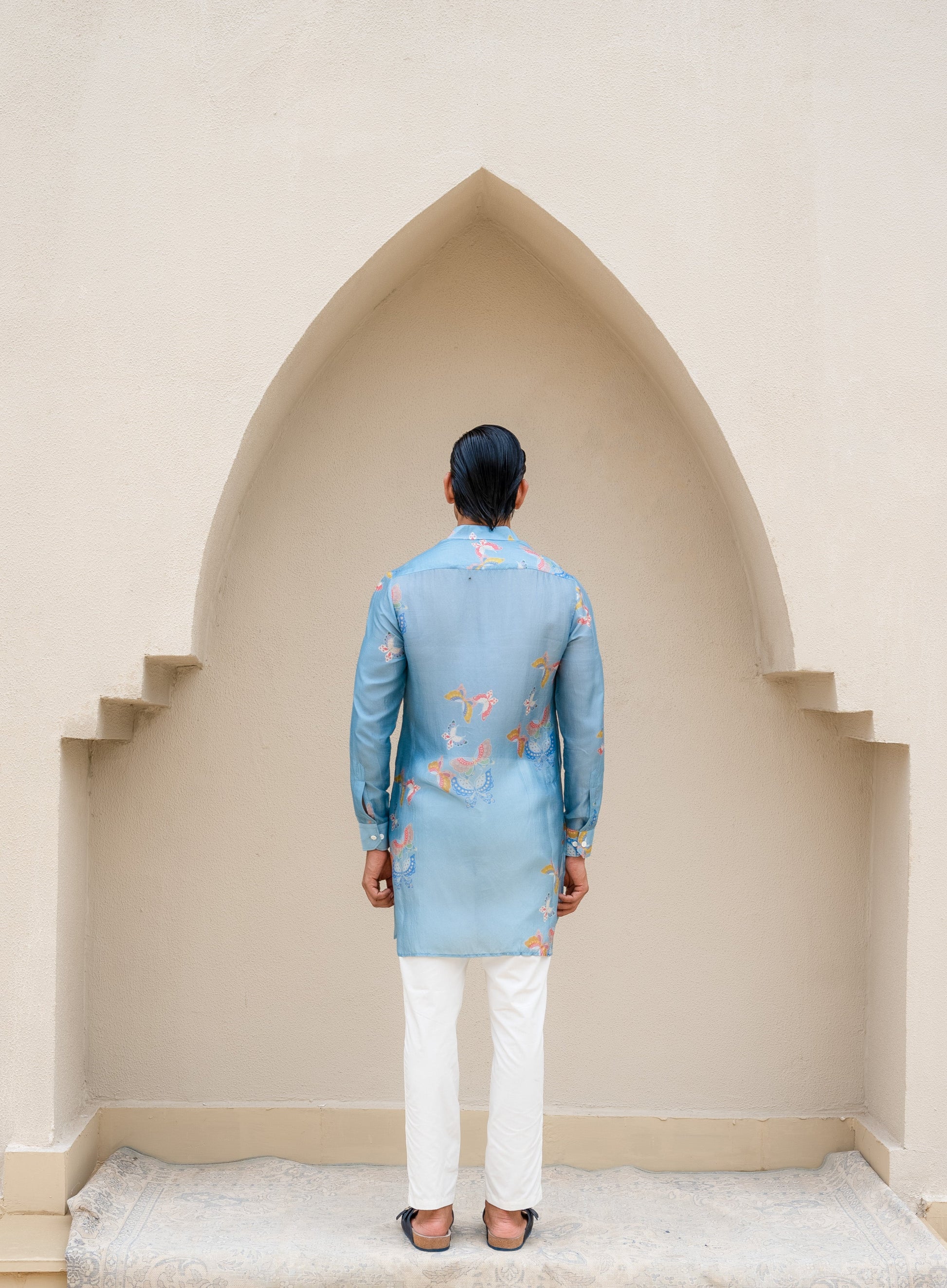 Men's printed kurta with butterfly design in blue fabric, styled with white trousers