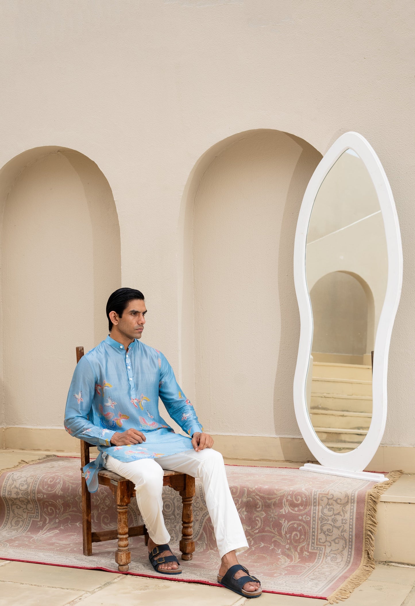 Men's printed kurta with butterfly design in blue worn by a model seated next to a mirror