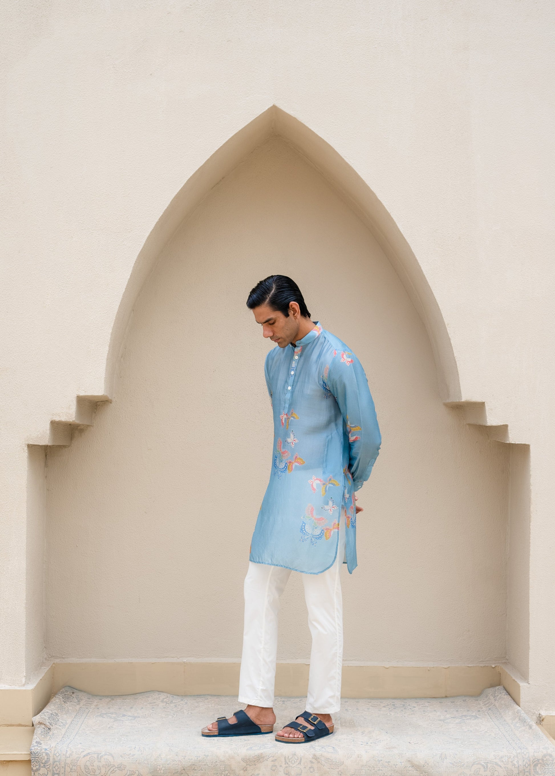 Men's printed kurta with butterfly design in soft blue, styled with white pants and sandals
