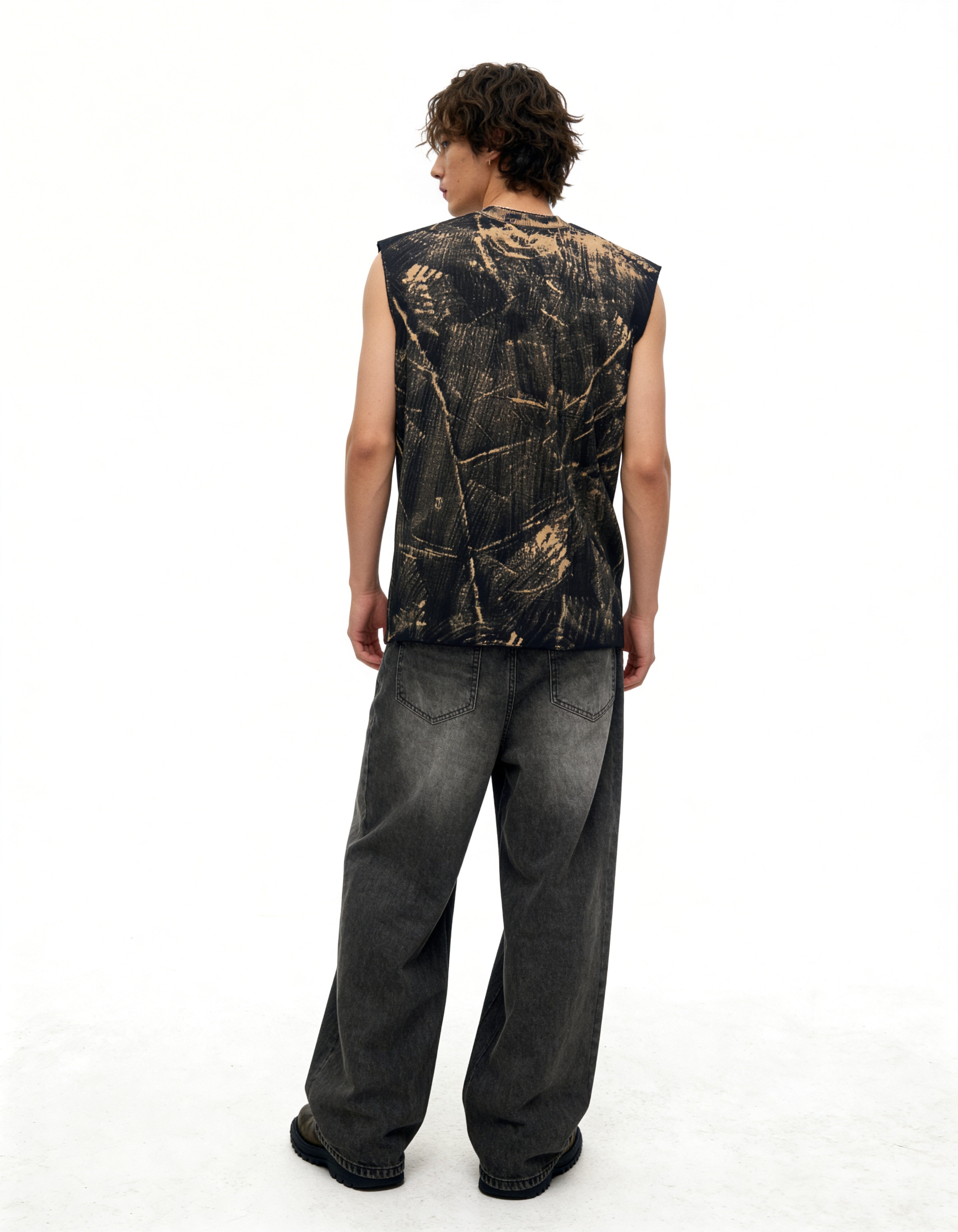 Person wearing a sleeveless camouflage shirt and dark jeans on a white background