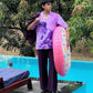 Model by pool wearing purple printed short sleeve shirt and tailored pants holding inflatable donut men's trendy summer shirts