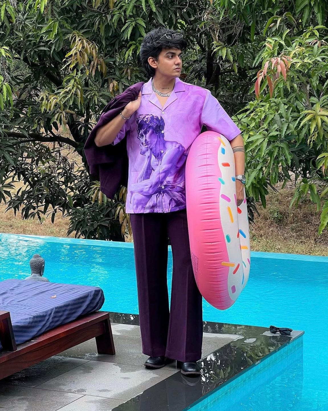 Model by pool wearing purple printed short sleeve shirt and tailored pants holding inflatable donut men's trendy summer shirts