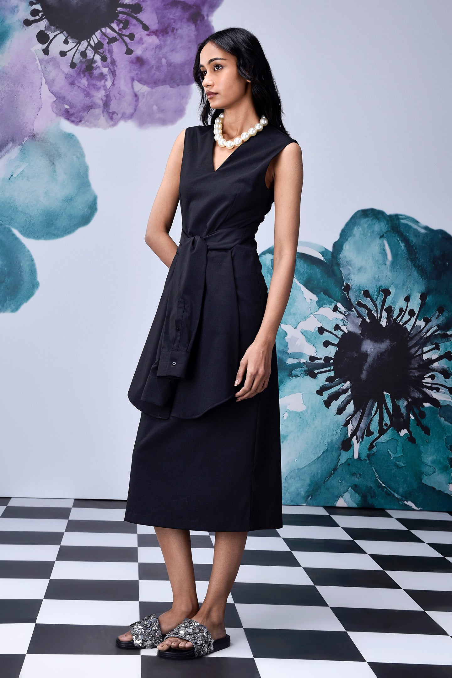 Model in Stylera midi black dress with belt V neck sleeveless styling pearl necklace and sandals