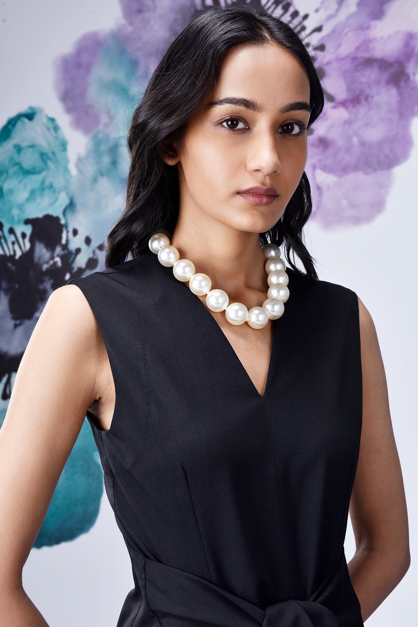 Model wearing Stylera midi black dress with belt V neck sleeveless style and pearl necklace
