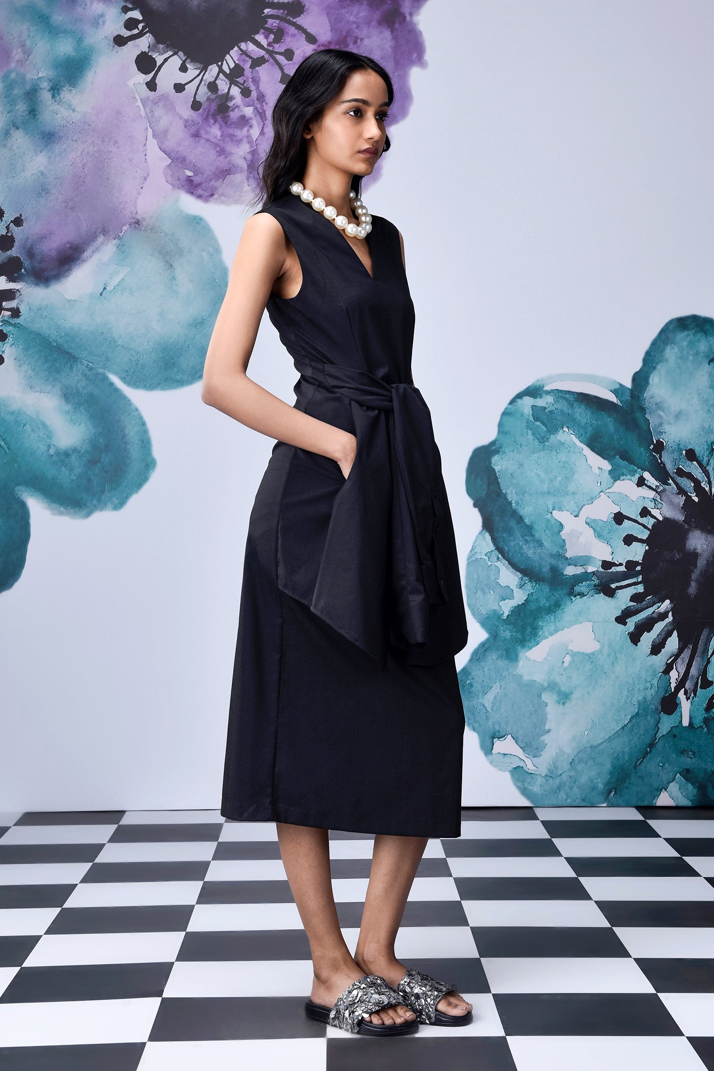 Stylera model wearing a sleeveless midi black dress with belt and side pockets