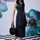 Stylera model wearing midi black dress with belt side tie V neck sleeveless with pearl necklace and black handbag