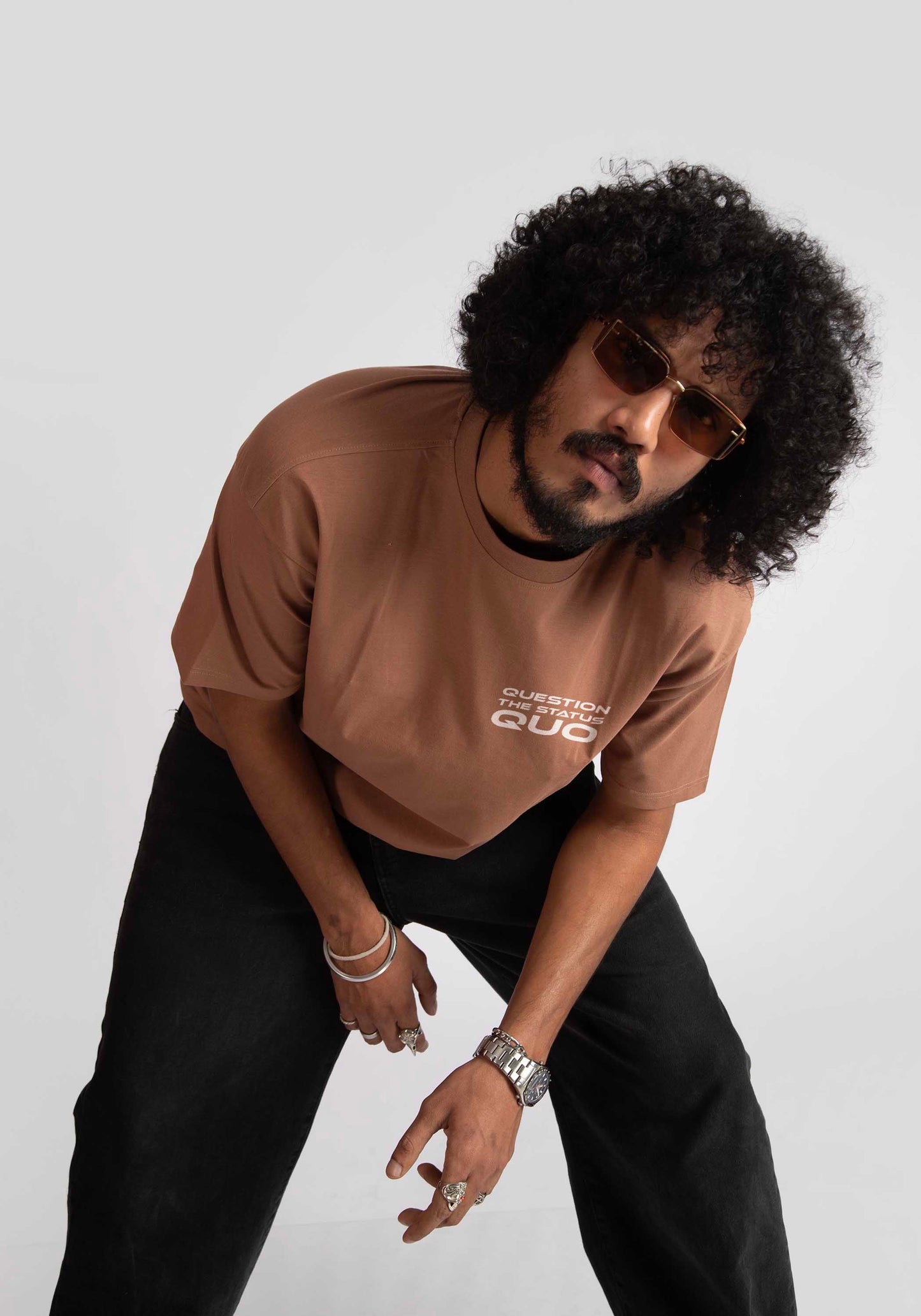 Man wearing mocha oversized t-shirt with white print paired with black pants and sunglasses