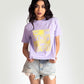 Stylera Woman wearing lavender graphic t-shirt for women with yellow floral design and distressed denim shorts