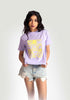 Stylera Woman wearing lavender graphic t-shirt for women with yellow floral design and distressed denim shorts