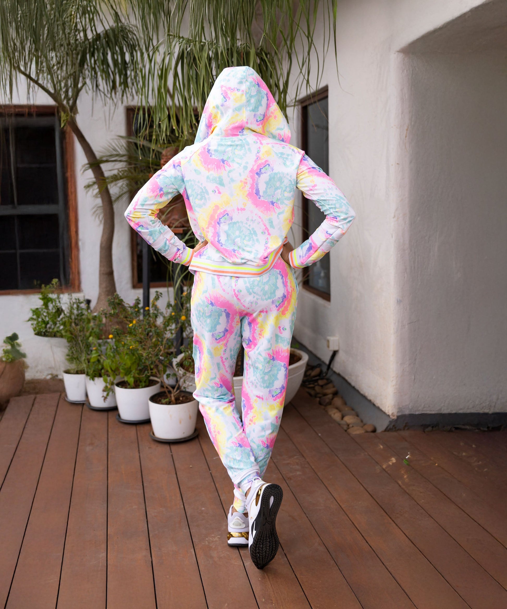 Back view of a woman wearing a multicolor neon jacket and joggers set with a hood and a colorful design