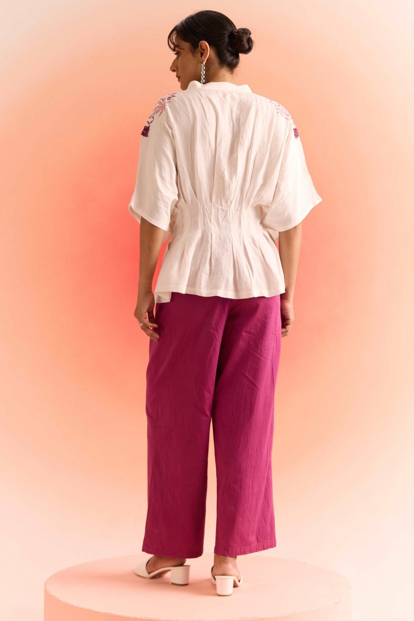 Woman wearing off white embroidered cord set top with wide sleeves paired with magenta wide-leg pants