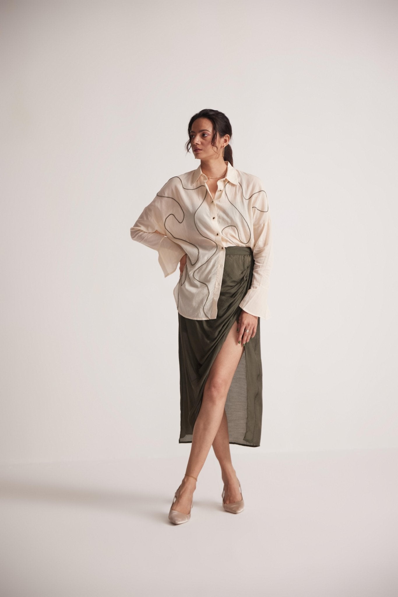 Stylera off-white oversized cotton shirt styled with olive green high slit skirt and beige heels