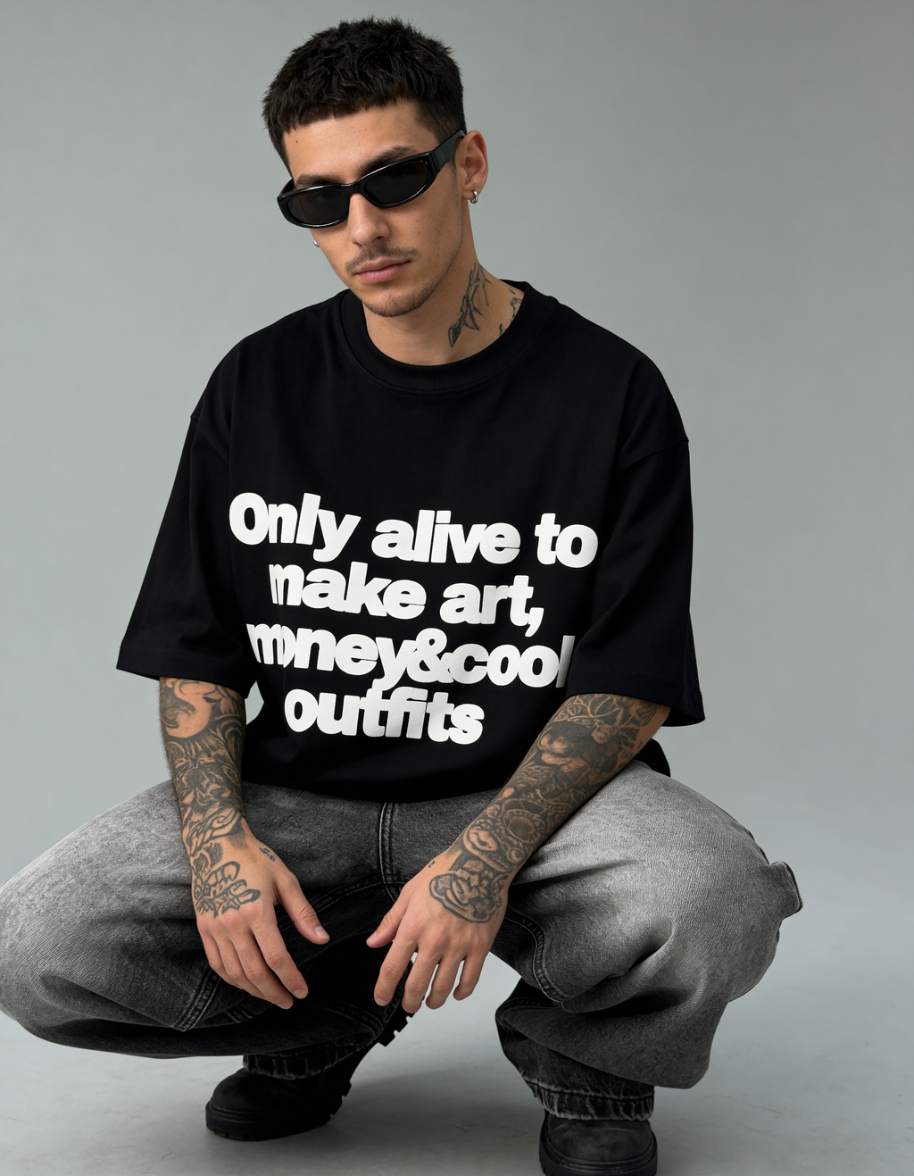 Man wearing a black t-shirt with text, sitting on the ground against a gray background