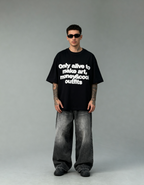 Person wearing a black t-shirt with text and gray pants on a gray background
