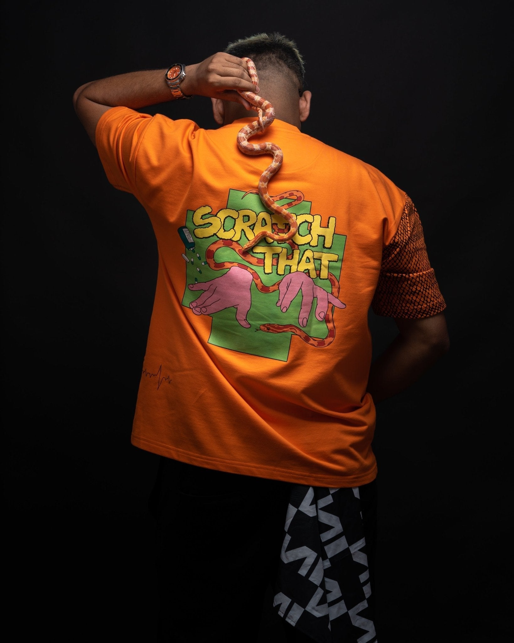 Stylera oversized orange streetwear tee shown from back with bold Scratch That graphic and snake accessory