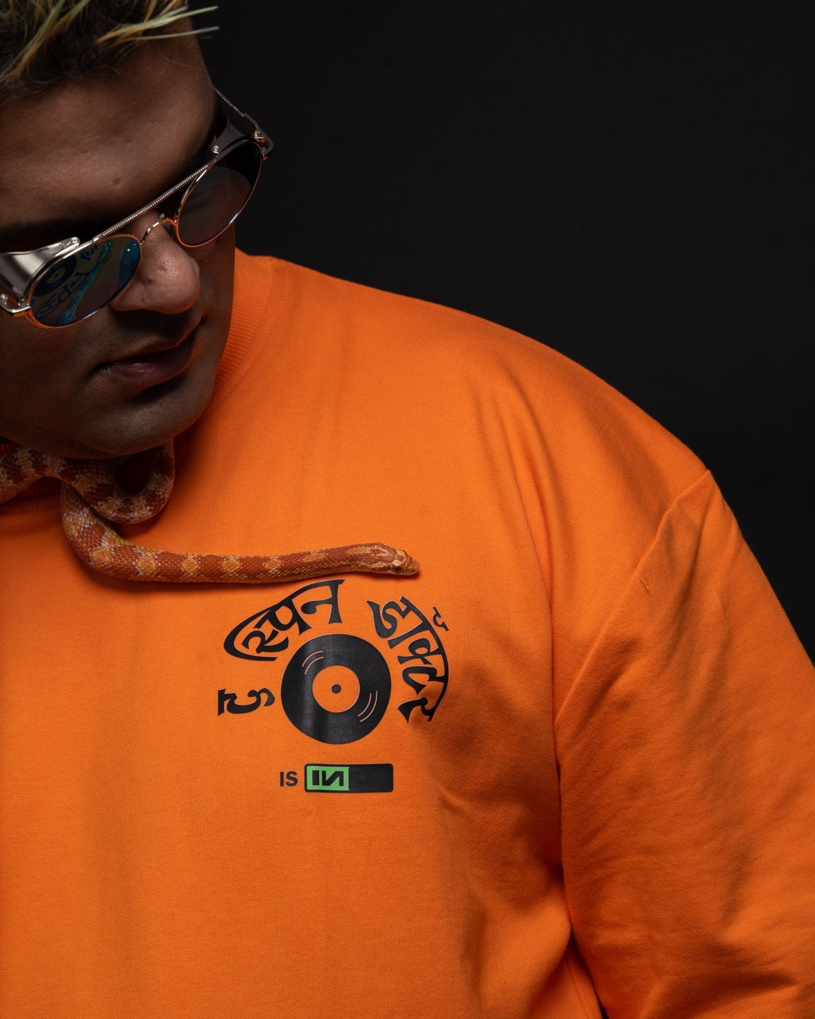 Stylera oversized orange streetwear tee with vinyl record chest graphic worn by model with snake and sunglasses