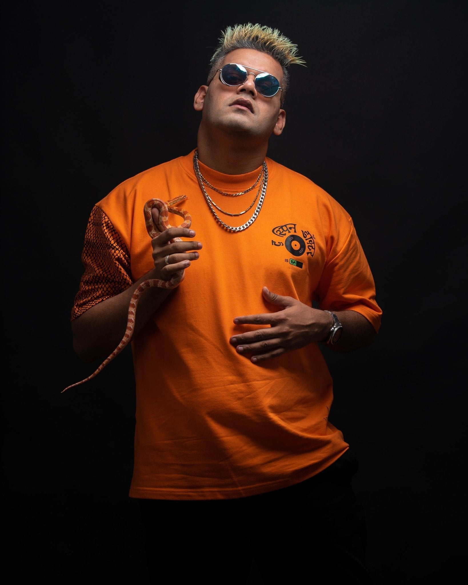 Stylera oversized orange streetwear tee on male model with sunglasses and layered chains holding a small snake