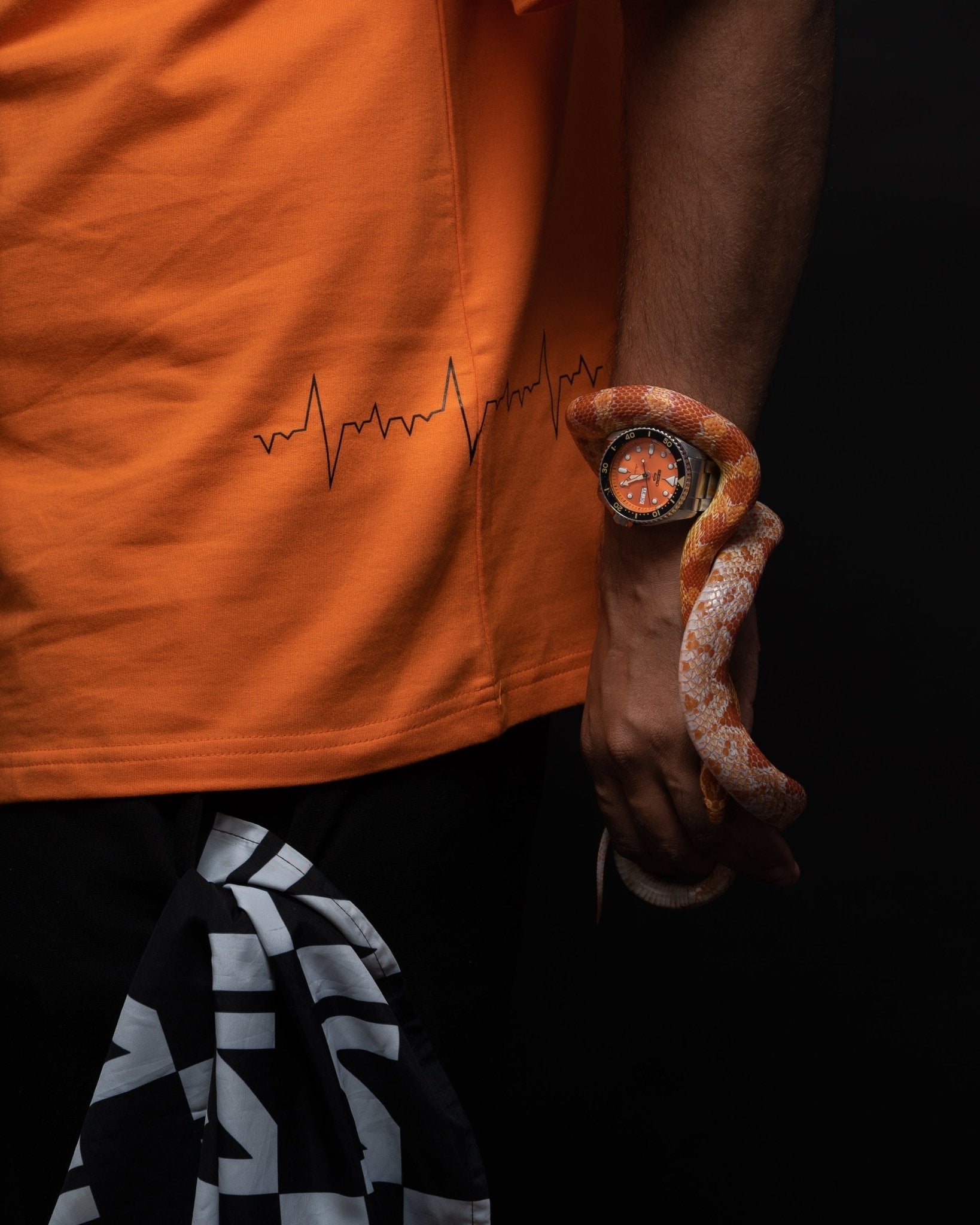 Stylera oversized orange streetwear tee with heartbeat stitch print worn by model holding corn snake and orange watch