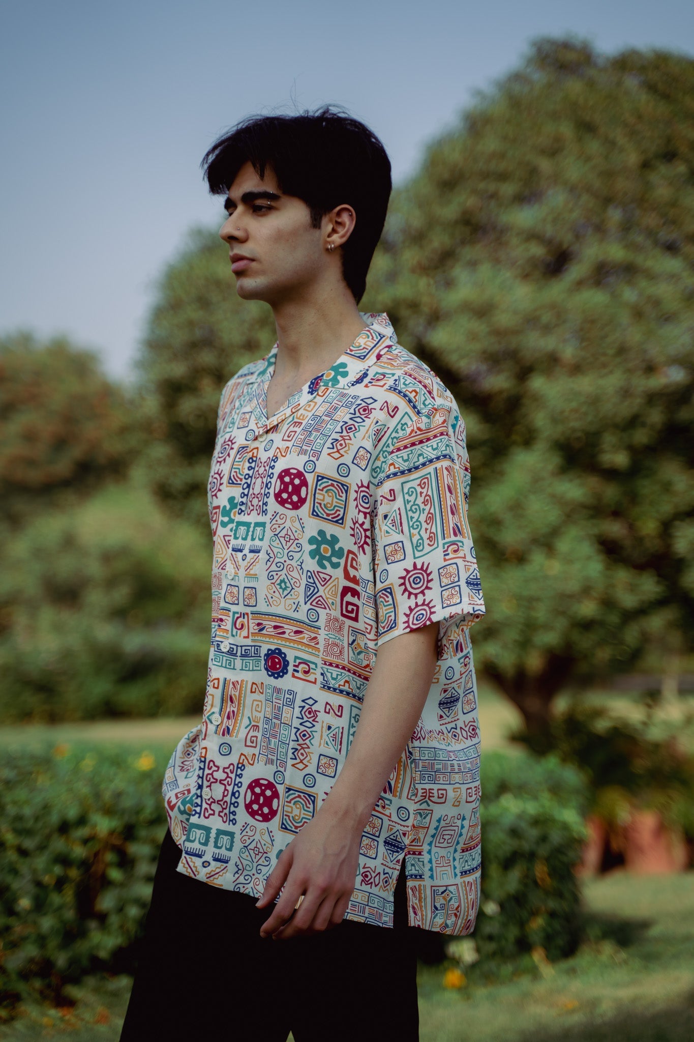 Model wearing an oversized casual summer shirt with colorful patterns in a lush outdoor setting