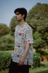 Model wearing an oversized casual summer shirt with colorful patterns in a lush outdoor setting