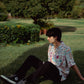 Model sitting on grass wearing an oversized casual summer shirt from Stylera 