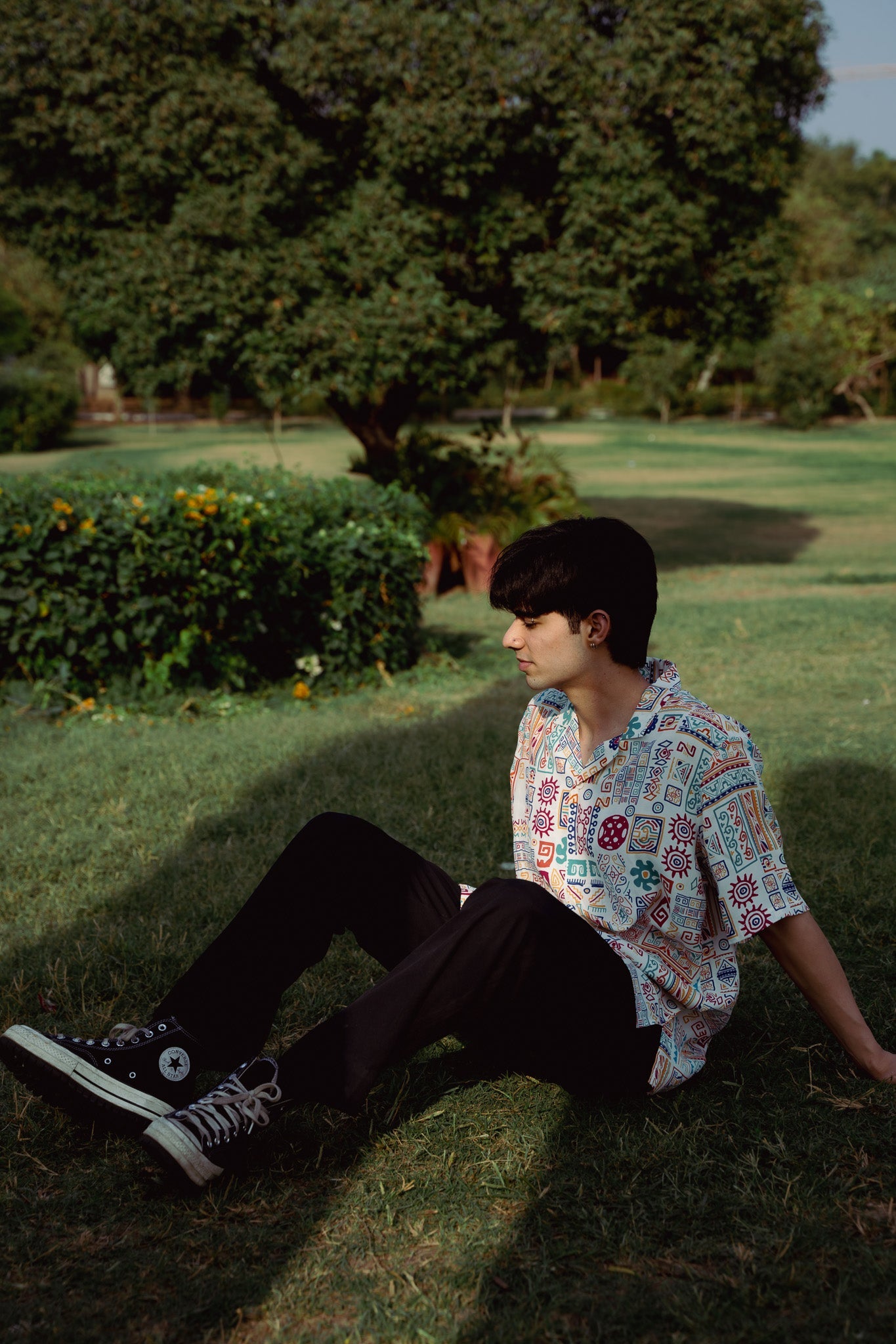 Model sitting on grass wearing an oversized casual summer shirt from Stylera 
