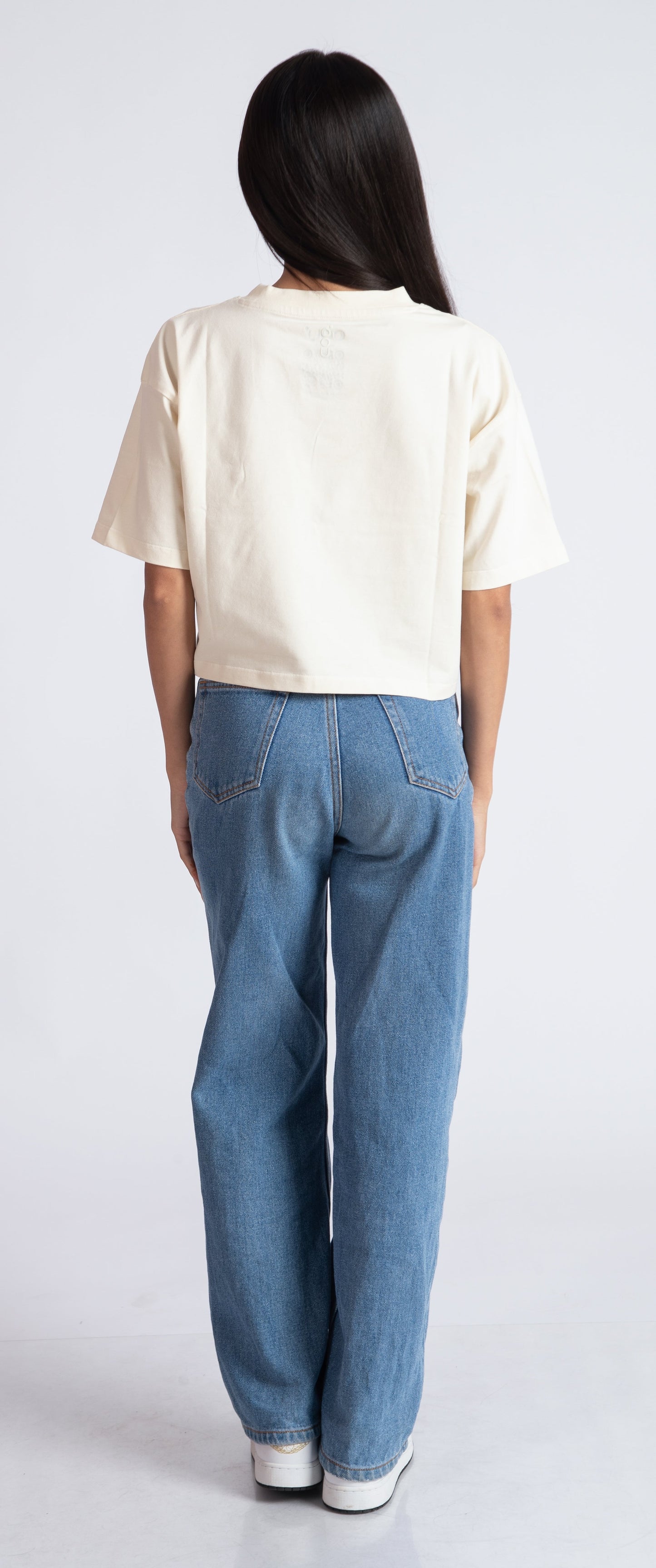 Back view of woman wearing oversized crop top for women in cream color paired with blue jeans