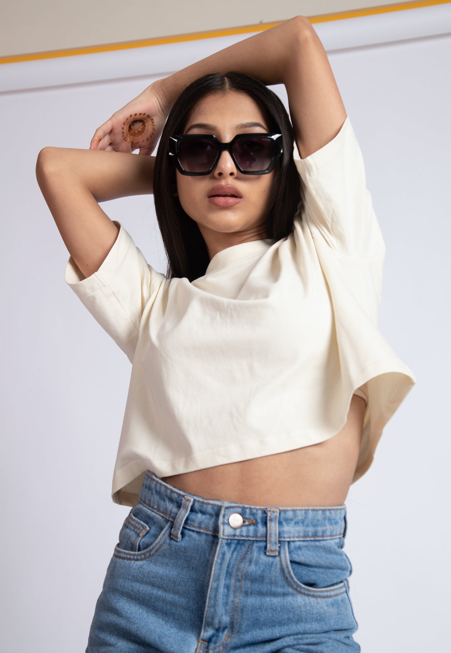 Woman wearing oversized crop top for women in white paired with high waist blue jeans and sunglasses
