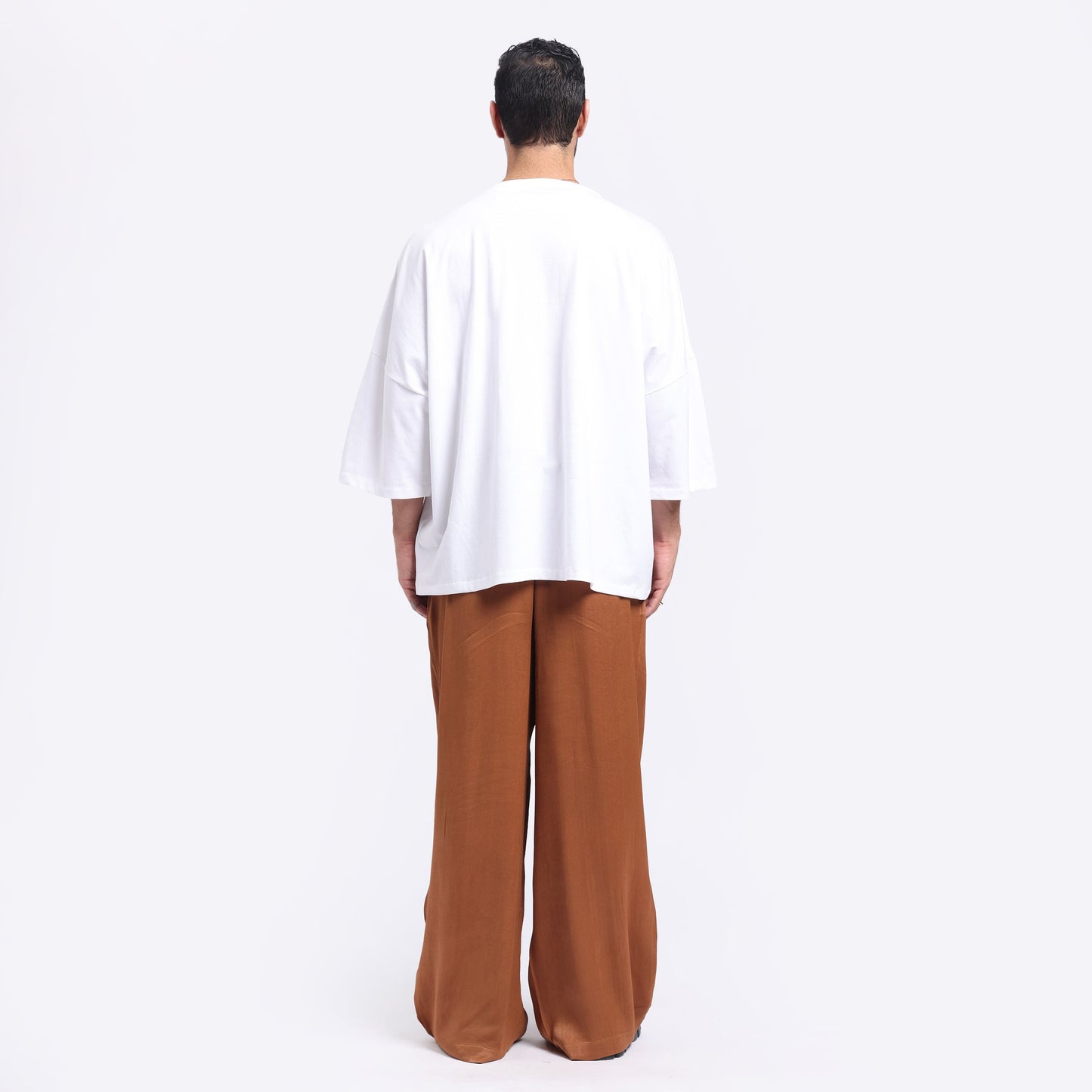 Back view of oversized white tee men paired with brown wide-leg pants for a casual look