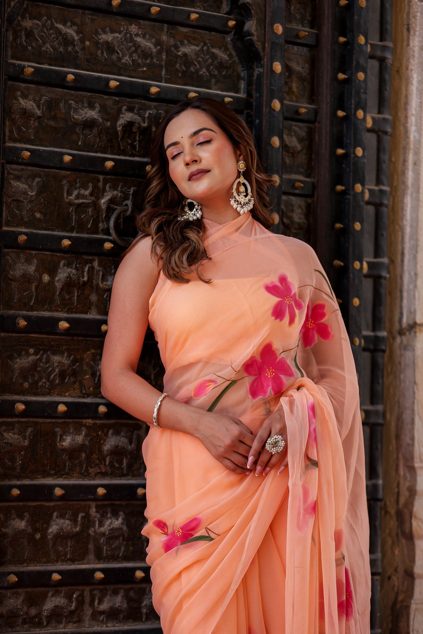 Stylera peach chiffon saree with floral design draped elegantly on a model against a vintage backdrop
