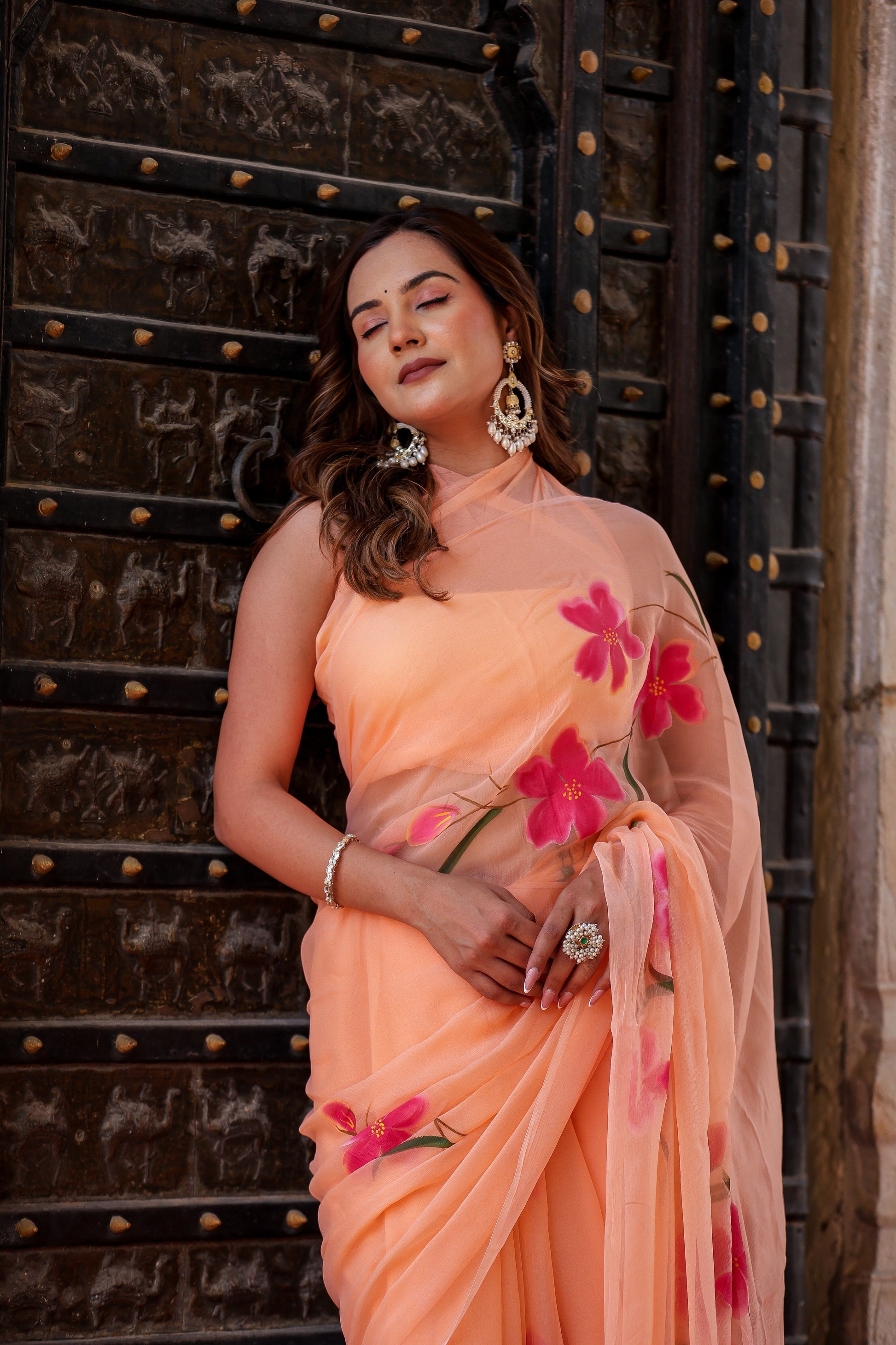 Stylera peach chiffon saree with floral design draped elegantly on a model against a vintage backdrop
