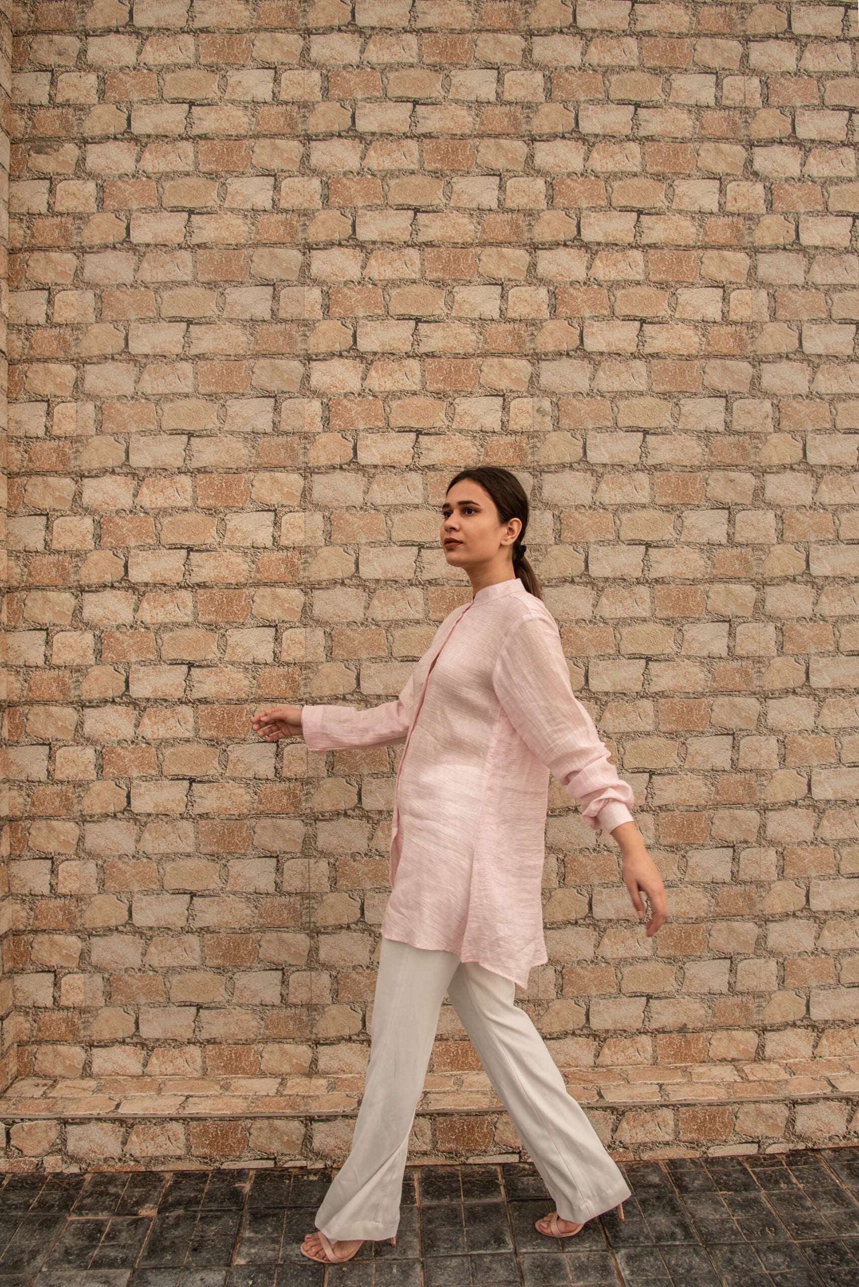 Woman wearing a pink linen top outfit shirt by Stylera paired with white pants walking outdoors