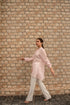Woman wearing a pink linen top outfit shirt by Stylera paired with white pants walking outdoors