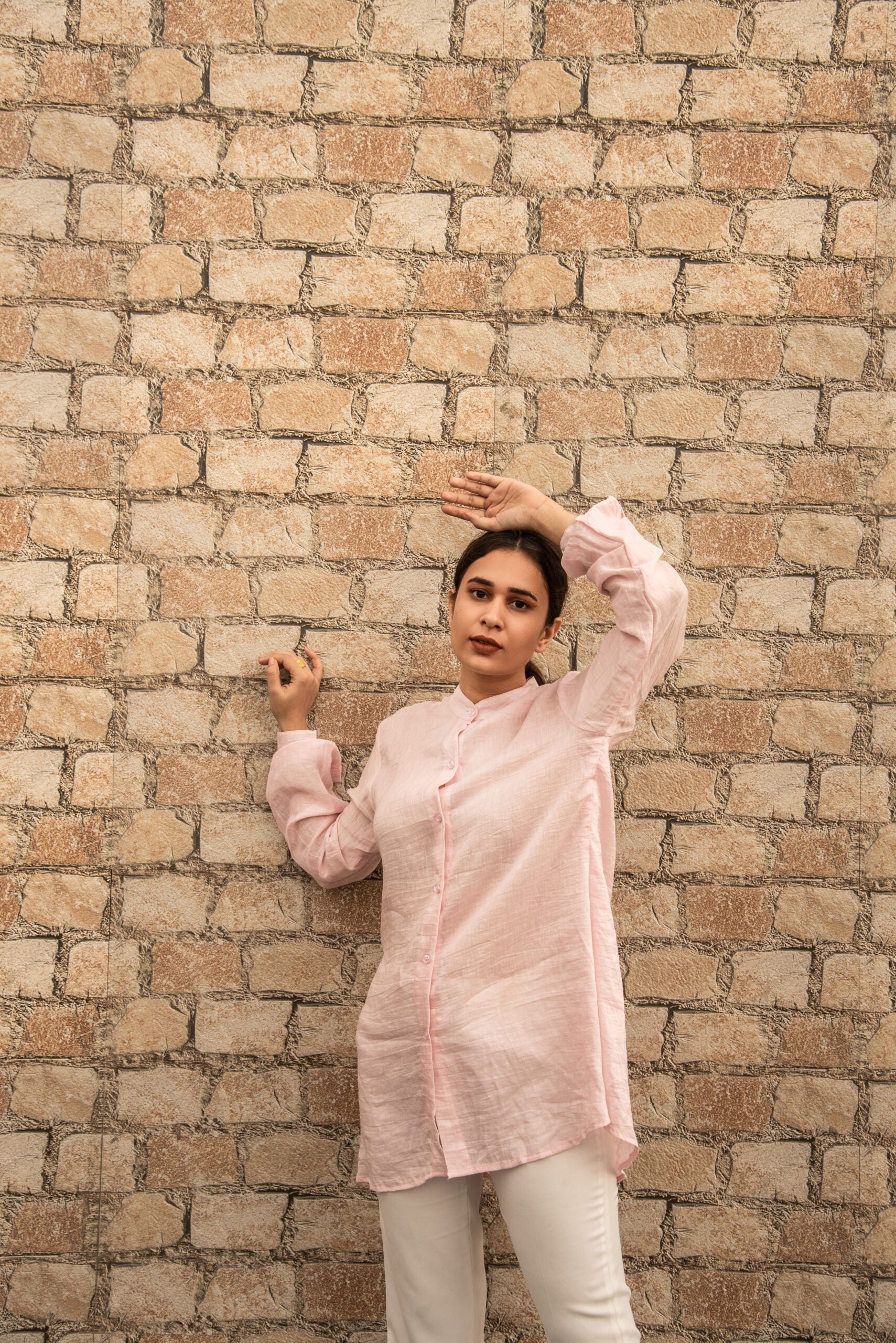 Woman wearing a pink linen top outfit by Stylera standing against a brick wall background