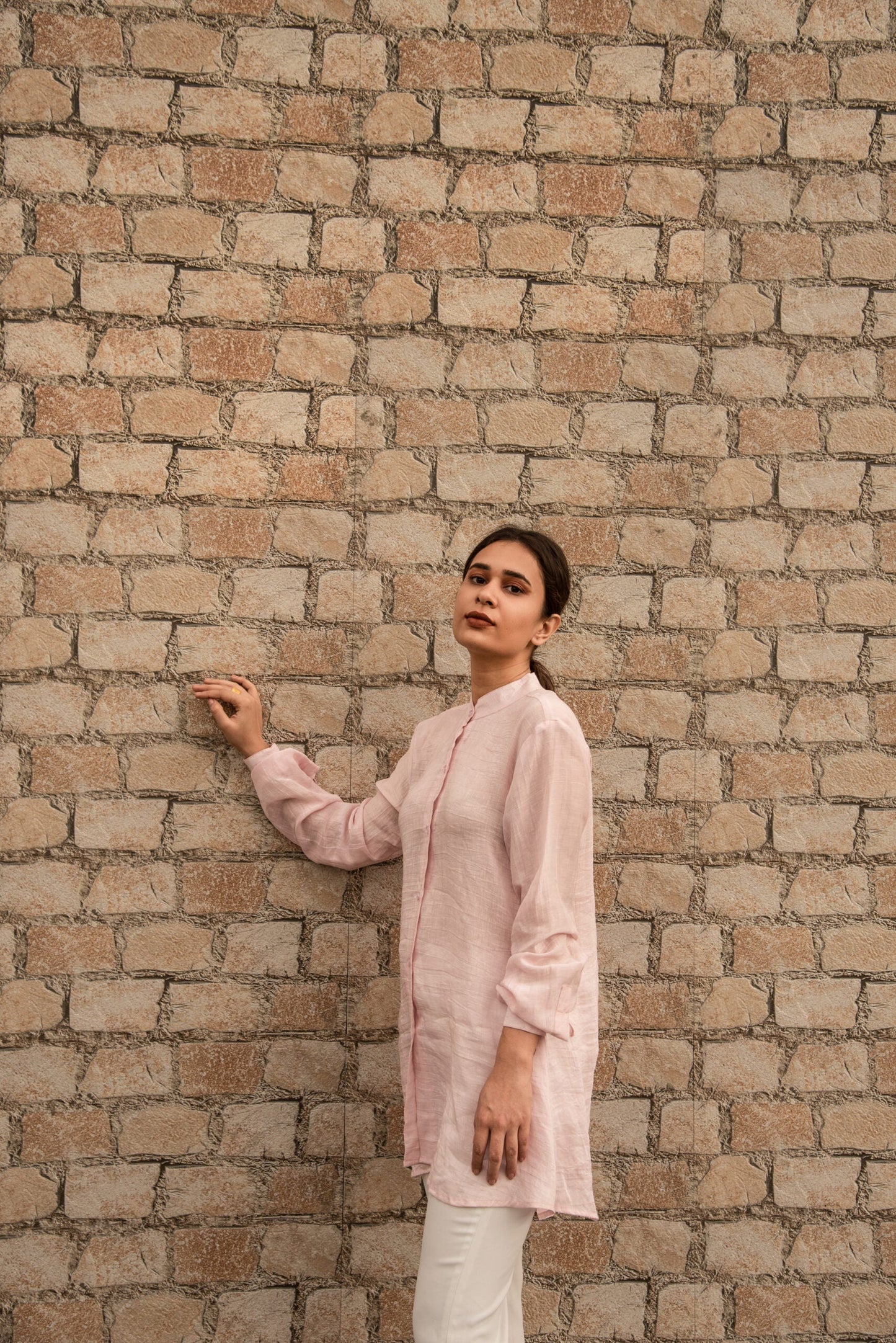 Woman wearing a pink linen top outfit by Stylera standing against a brick wall
