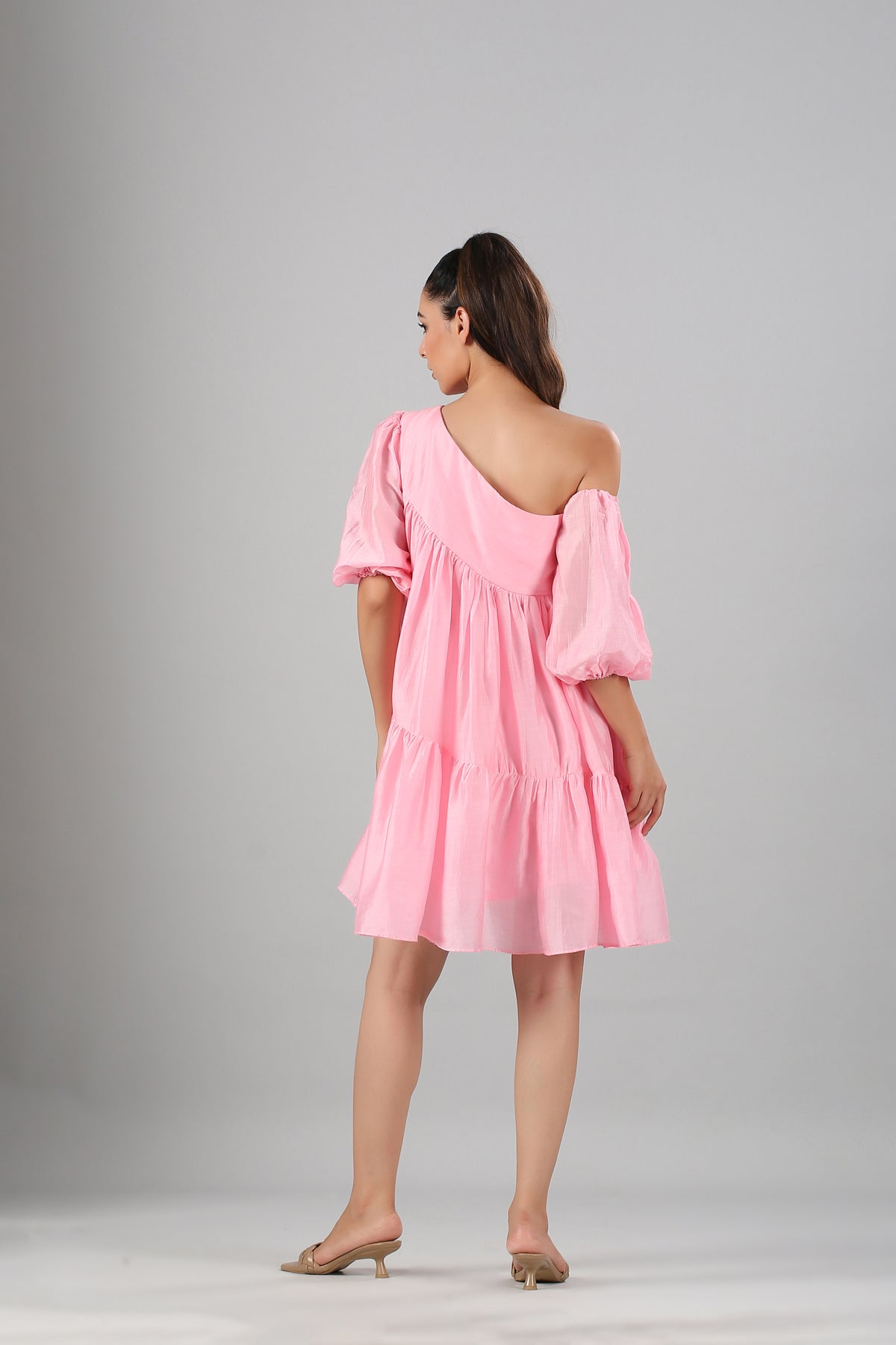 Model wearing Stylera pink off shoulder dress back view tiered mini with puff sleeves and one shoulder detail