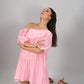Model kneeling in studio wearing pink off shoulder dress with puff sleeves and tiered skirt looking upward