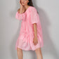 Stylera model wearing pink off shoulder dress tiered short silhouette with puff sleeves and relaxed fit