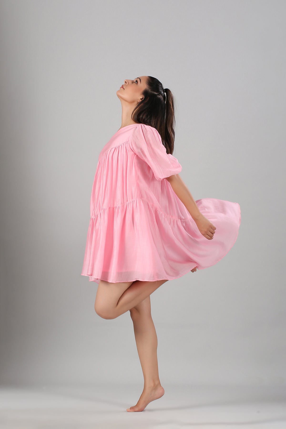 Stylera pink off shoulder dress loose tiered babydoll style on model mid twirl barefoot studio