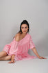 Stylera model seated on studio floor wearing pink off shoulder dress with relaxed sleeves and summer casual style