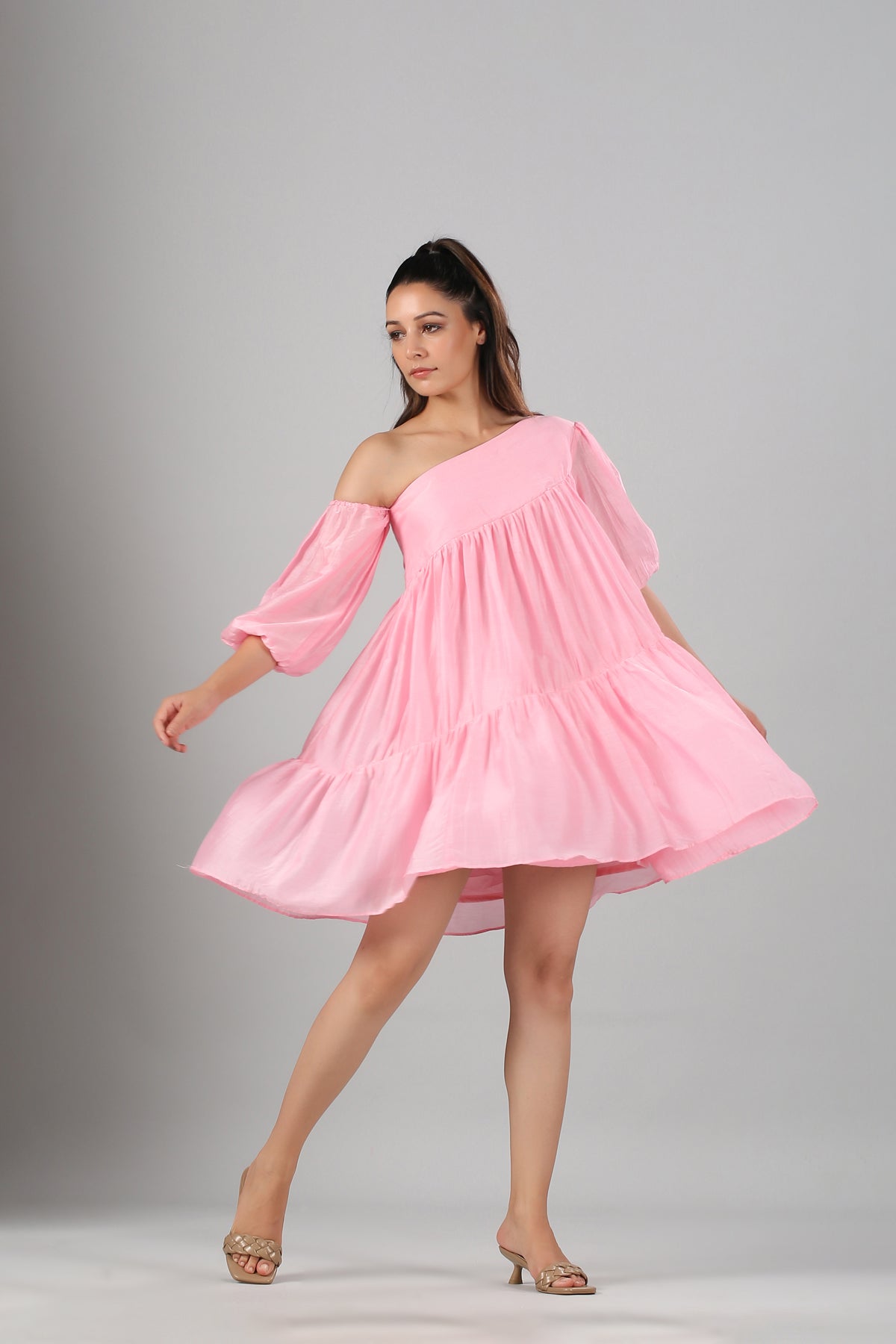 Model wearing pink off shoulder dress with tiered skirt and puff sleeves twirling in nude heels