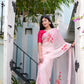 Elegant pink saree for women with floral embroidery, worn by a model standing in a stylish entrance.