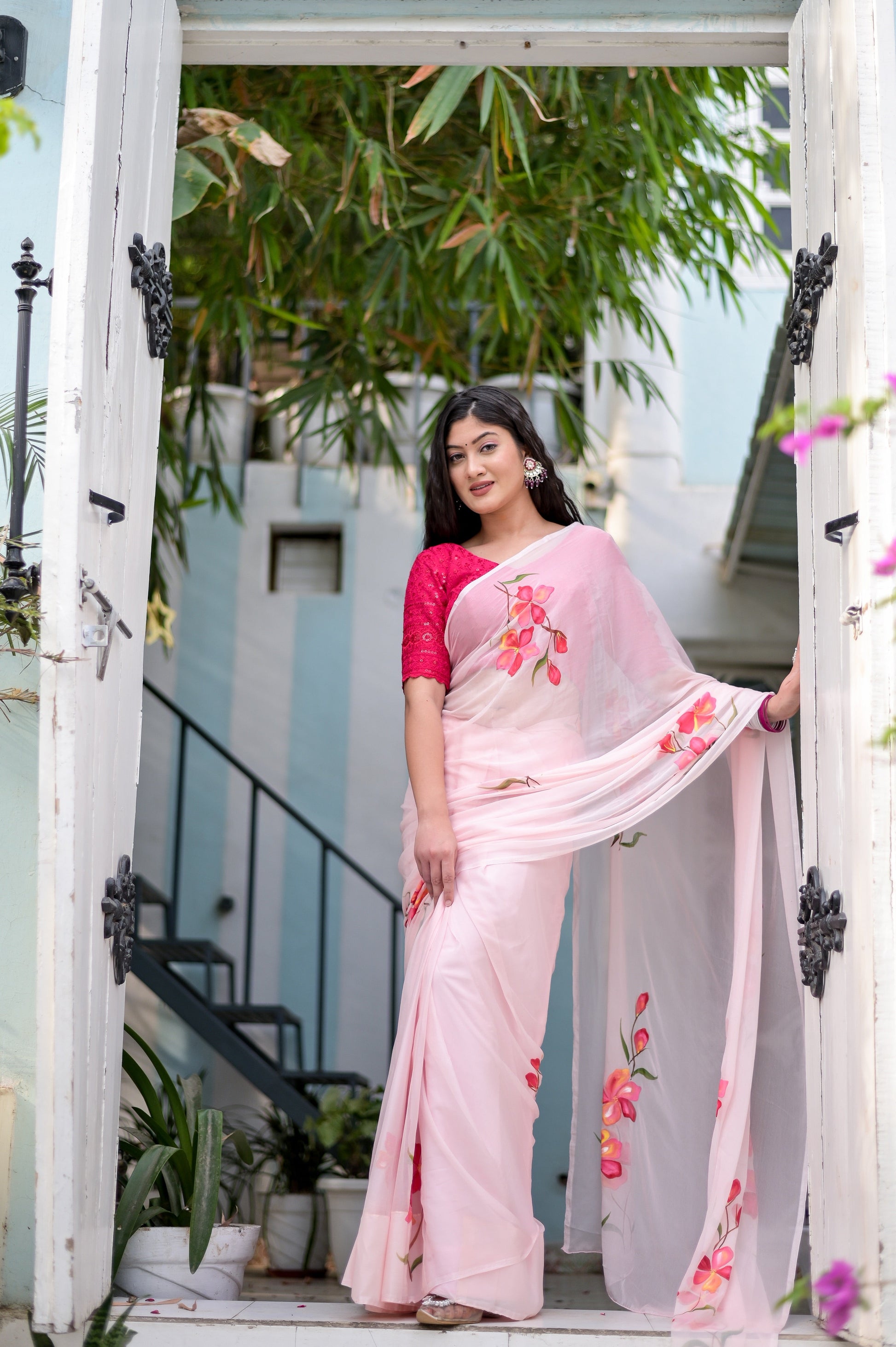 Elegant pink saree for women with floral embroidery, worn by a model standing in a stylish entrance.
