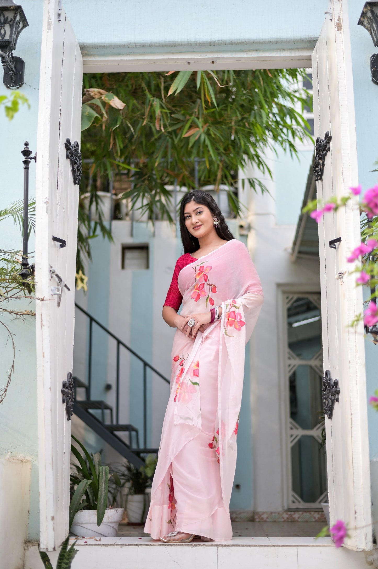 Elegant pink saree for women with floral embroidery, worn by a model at a picturesque entrance