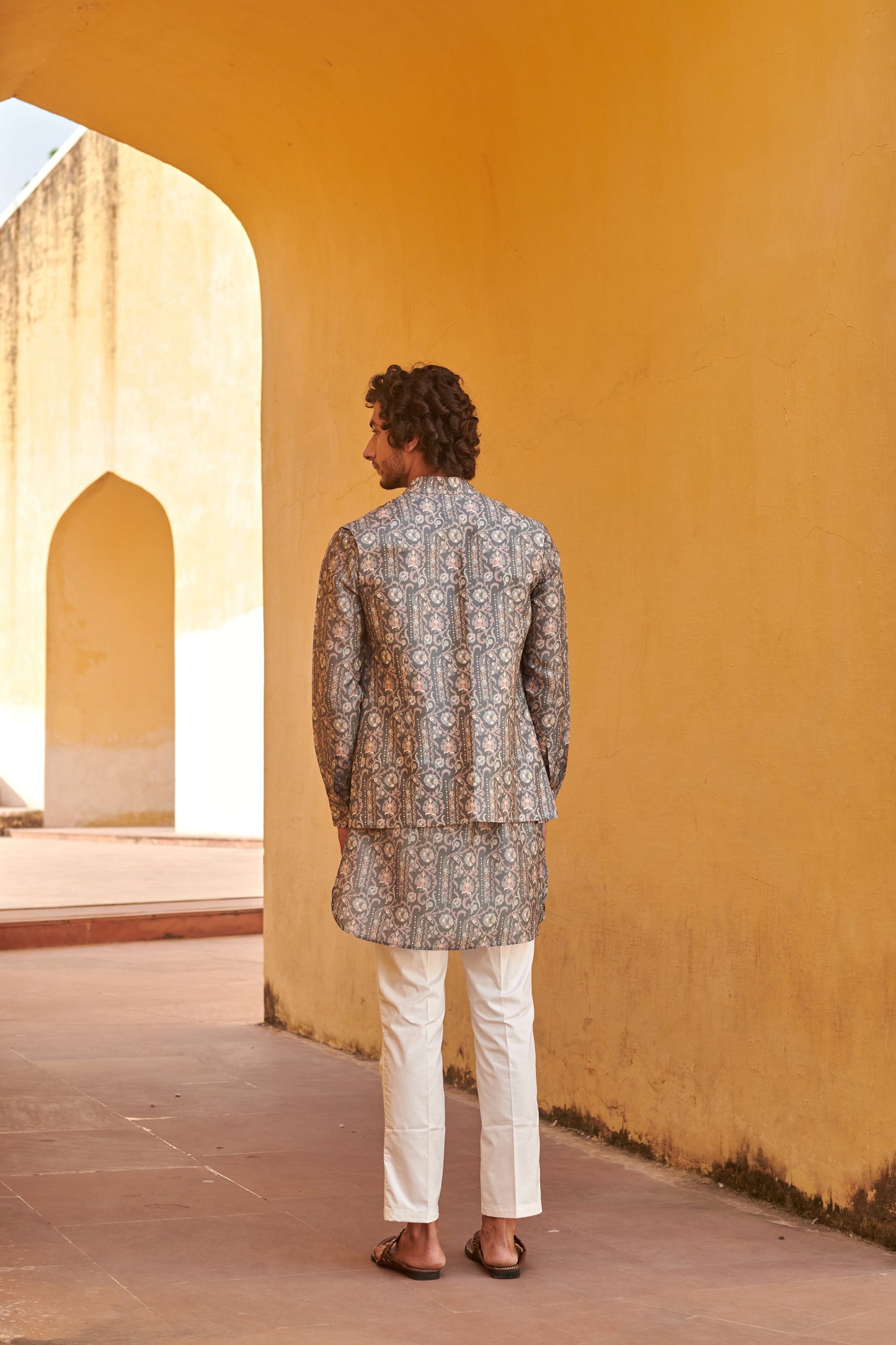 Man wearing a stylish printed kurta and jacket for men with intricate patterns, set in a vibrant archway