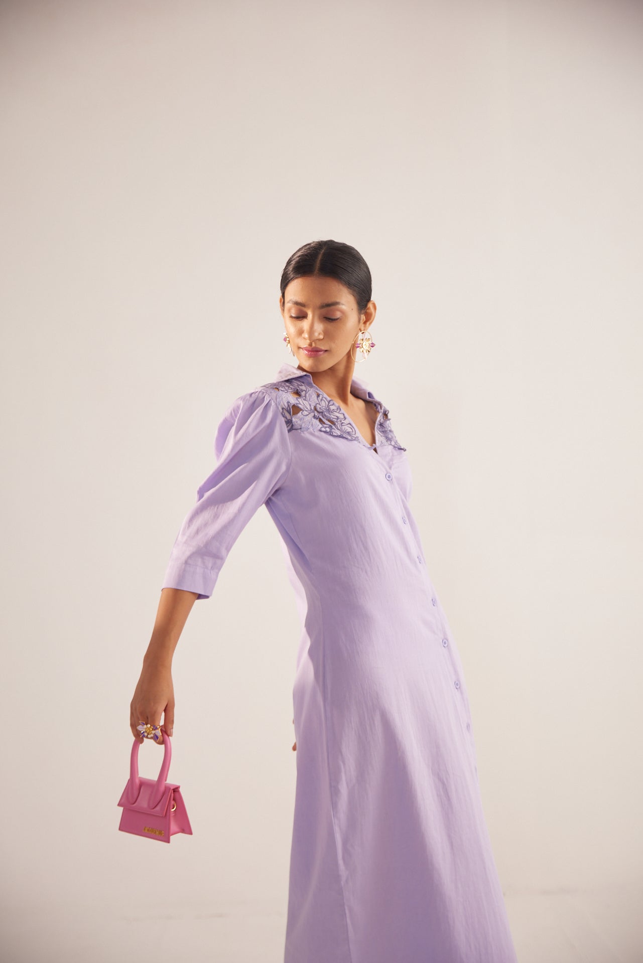 Stylera purple embroidered event dress with three-quarter sleeves worn by model holding a small pink handbag