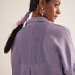 Back view of a woman wearing a purple oversized cotton shirt by Stylera with detailed pleats on the back